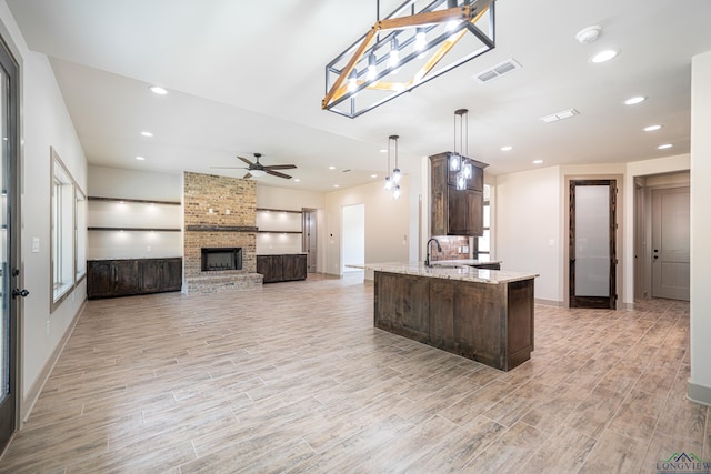 kitchen with light stone counters, dark brown cabinets, a large fireplace, ceiling fan, and hanging light fixtures