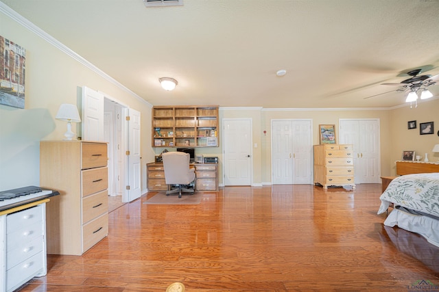 bedroom with ceiling fan, wood-type flooring, crown molding, and multiple closets