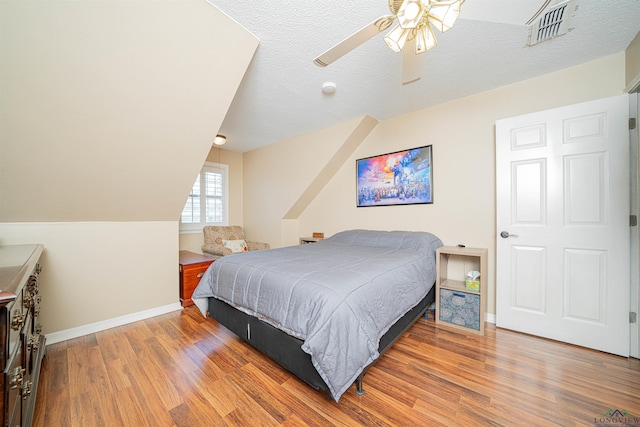 bedroom featuring ceiling fan, wood-type flooring, a textured ceiling, and lofted ceiling