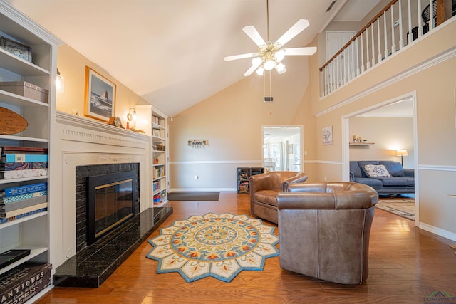 living room with hardwood / wood-style floors, lofted ceiling, built in shelves, a premium fireplace, and ceiling fan