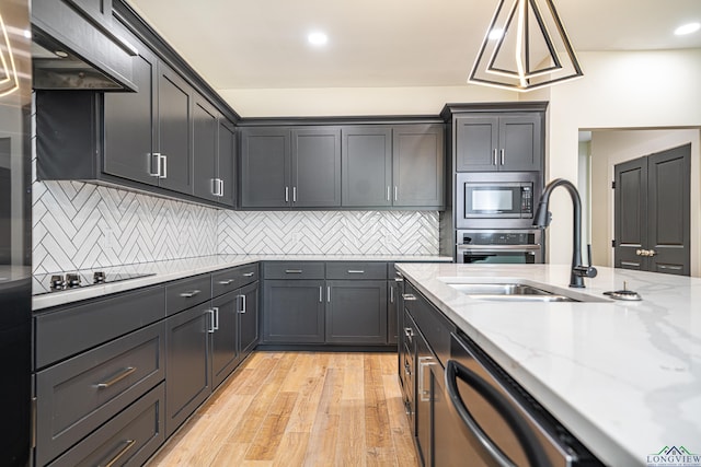 kitchen featuring pendant lighting, sink, light wood-type flooring, appliances with stainless steel finishes, and light stone counters