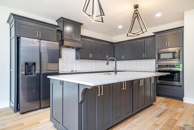 kitchen featuring sink, stainless steel appliances, light stone counters, an island with sink, and decorative light fixtures