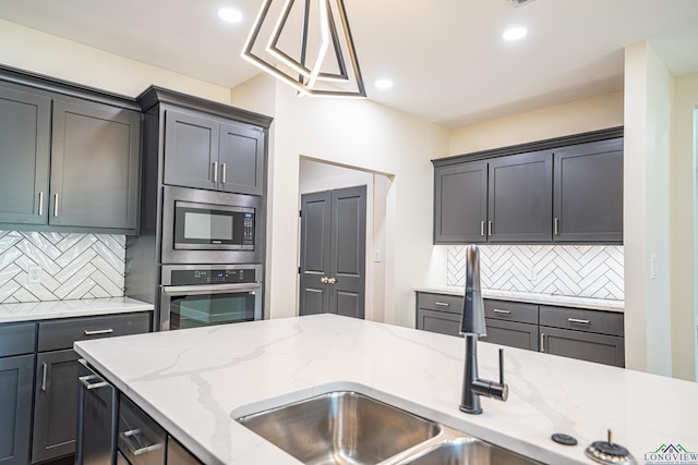 kitchen featuring backsplash, decorative light fixtures, light stone counters, and stainless steel appliances