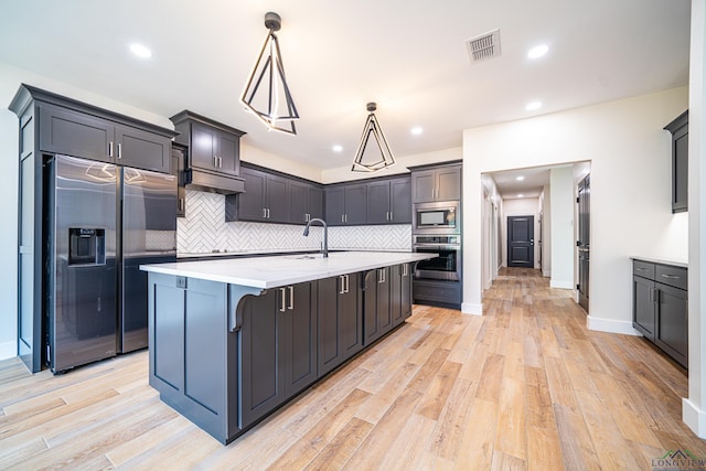 kitchen featuring pendant lighting, a kitchen island with sink, built in appliances, tasteful backsplash, and a breakfast bar area