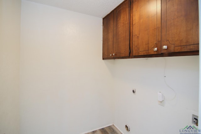 clothes washing area featuring a textured ceiling, electric dryer hookup, cabinet space, and wood finished floors