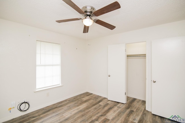 unfurnished bedroom featuring a textured ceiling, multiple windows, wood finished floors, and a closet