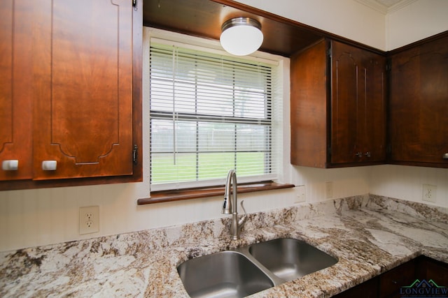 kitchen featuring dark brown cabinets, light stone countertops, and a sink