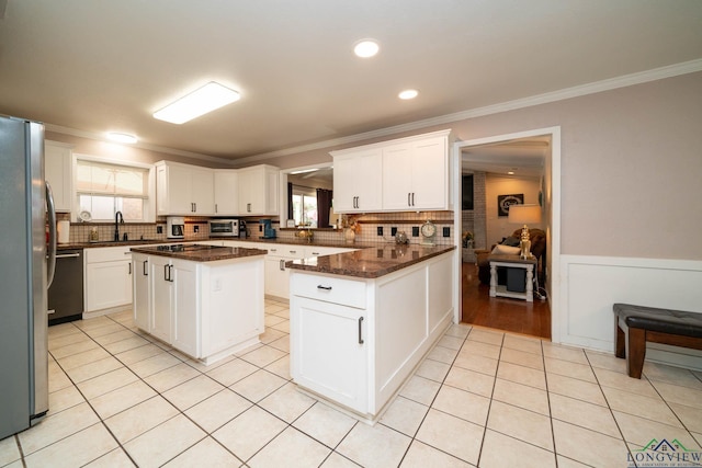 kitchen with white cabinets, ornamental molding, a kitchen island, and dark stone counters