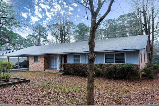 single story home with a carport, roof with shingles, board and batten siding, and brick siding