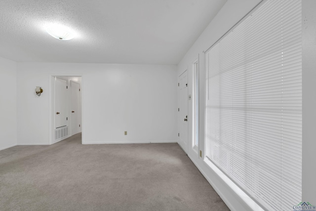 empty room featuring light carpet, a textured ceiling, and baseboards