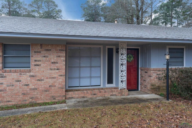 doorway to property with brick siding and roof with shingles