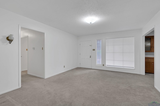 unfurnished room with a textured ceiling, carpet flooring, and baseboards