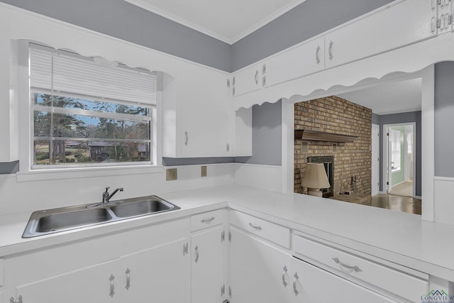 kitchen featuring white cabinets, ornamental molding, light countertops, a fireplace, and a sink