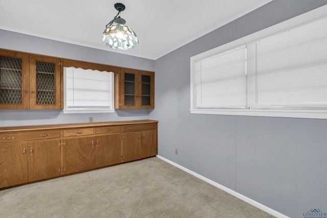 kitchen featuring glass insert cabinets, light carpet, baseboards, brown cabinets, and decorative light fixtures