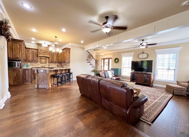 living room with dark wood-type flooring, ceiling fan with notable chandelier, and ornamental molding