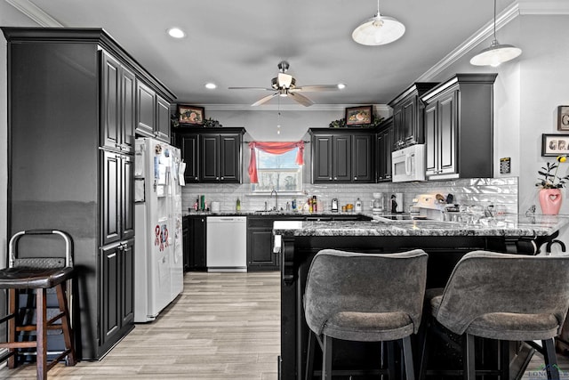 kitchen featuring a kitchen bar, sink, stone countertops, kitchen peninsula, and white appliances