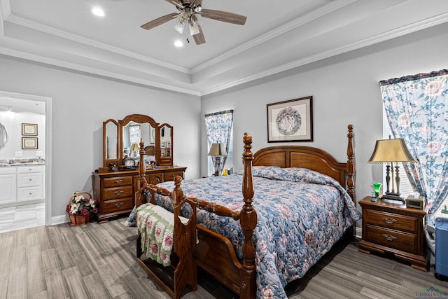 bedroom featuring ceiling fan, ensuite bathroom, ornamental molding, a raised ceiling, and light wood-type flooring