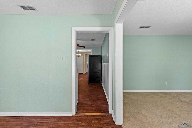 hall with dark carpet and a textured ceiling