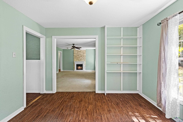 spare room with dark hardwood / wood-style floors, a large fireplace, and ceiling fan