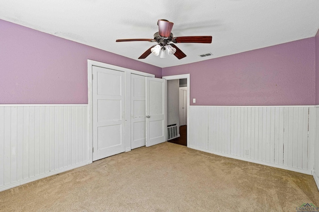 unfurnished bedroom with light carpet, ceiling fan, and multiple closets