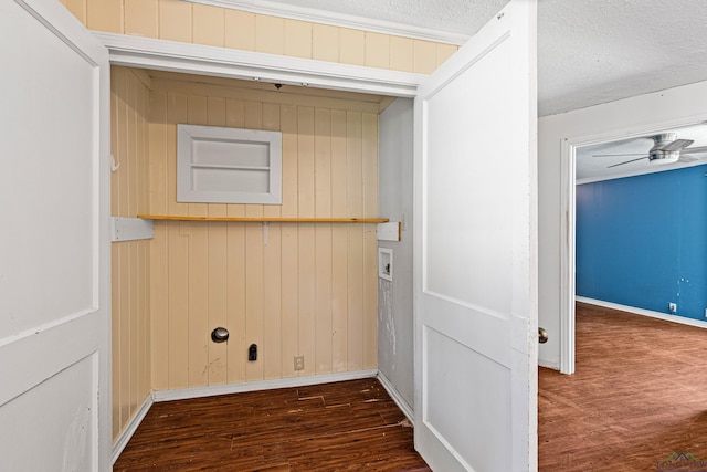 clothes washing area featuring a textured ceiling, ceiling fan, dark wood-type flooring, and wood walls