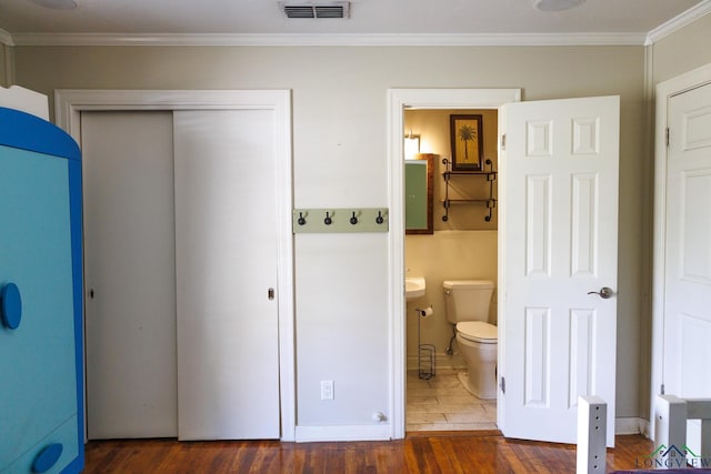 bedroom featuring dark hardwood / wood-style flooring, ensuite bathroom, a closet, and crown molding