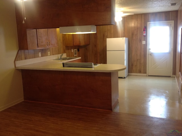 kitchen featuring kitchen peninsula, a textured ceiling, sink, white fridge, and wood walls