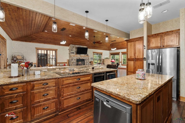 kitchen featuring ceiling fan, a center island, hanging light fixtures, a stone fireplace, and appliances with stainless steel finishes