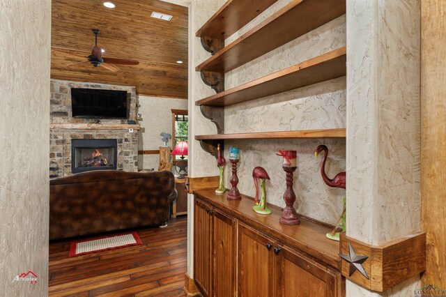 interior space with a stone fireplace, ceiling fan, wood ceiling, and dark hardwood / wood-style floors