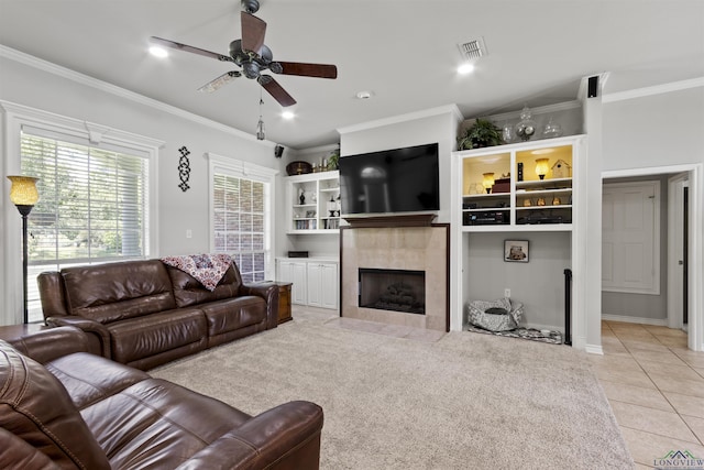 living room featuring ceiling fan, light colored carpet, ornamental molding, and a tiled fireplace