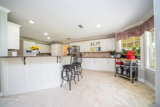 kitchen with white microwave, white cabinets, a kitchen bar, kitchen peninsula, and dark stone counters