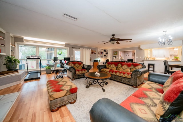 living room featuring light wood-type flooring, ceiling fan with notable chandelier, and built in features