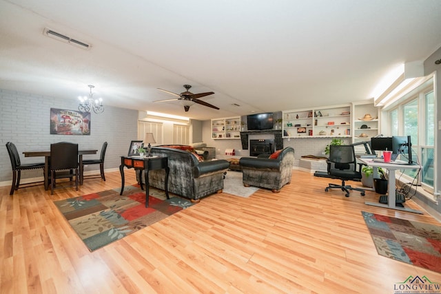 living room featuring brick wall, ceiling fan with notable chandelier, and light hardwood / wood-style floors