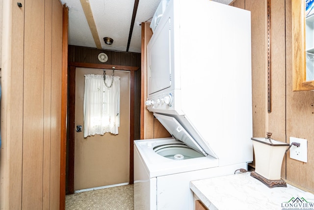 washroom featuring a textured ceiling, wooden walls, light carpet, and stacked washer / drying machine