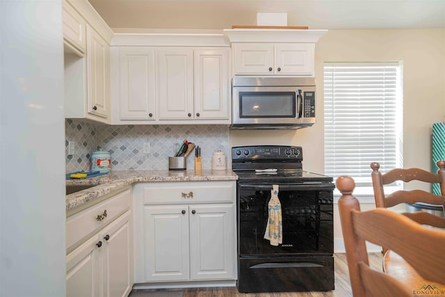 kitchen with stainless steel microwave, electric range, backsplash, white cabinets, and light stone countertops
