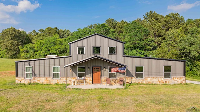 view of front of home with board and batten siding, a patio area, stone siding, and a front lawn
