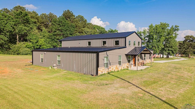 rear view of house with metal roof, a yard, stone siding, and a patio