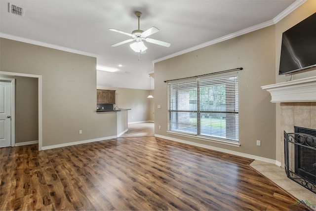 unfurnished living room with a tiled fireplace, crown molding, dark hardwood / wood-style floors, and ceiling fan