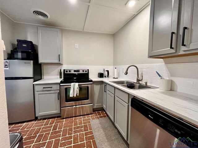16 Pegues Pl, Longview, TX 75601 - kitchen featuring stainless steel appliances, gray cabinetry, backsplash, and brick patterned floors