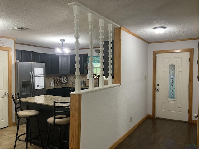 kitchen featuring an inviting chandelier, stainless steel refrigerator with ice dispenser, ornamental molding, a textured ceiling, and a kitchen bar