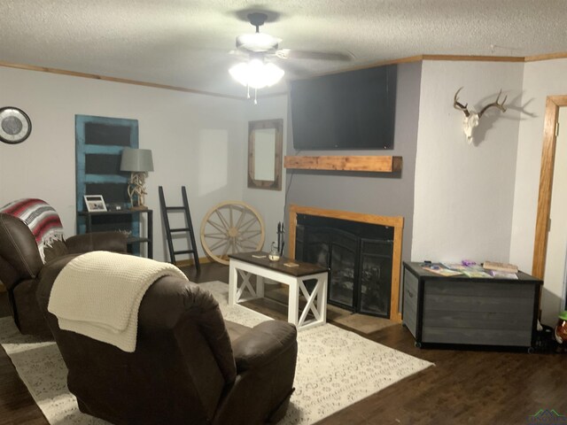 living room with ceiling fan, dark hardwood / wood-style flooring, a textured ceiling, and ornamental molding