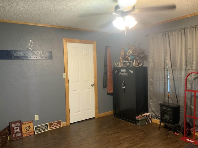 misc room with a textured ceiling, ceiling fan, dark wood-type flooring, crown molding, and a wood stove