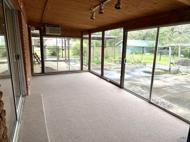 unfurnished sunroom with an AC wall unit, plenty of natural light, rail lighting, and wooden ceiling