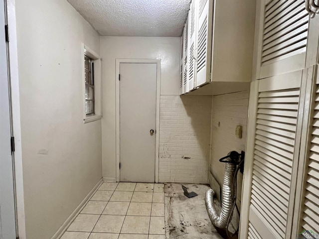 laundry area with light tile patterned floors, brick wall, and a textured ceiling