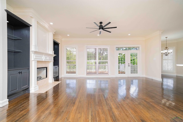 unfurnished living room featuring wood finished floors, baseboards, french doors, ceiling fan with notable chandelier, and a premium fireplace