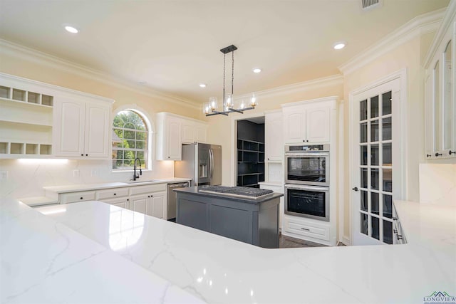 kitchen with crown molding, white cabinetry, light stone counters, a sink, and appliances with stainless steel finishes
