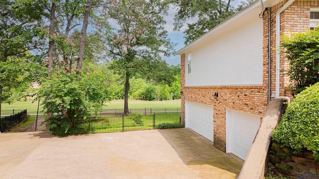 view of home's exterior with fence, an attached garage, brick siding, a lawn, and driveway