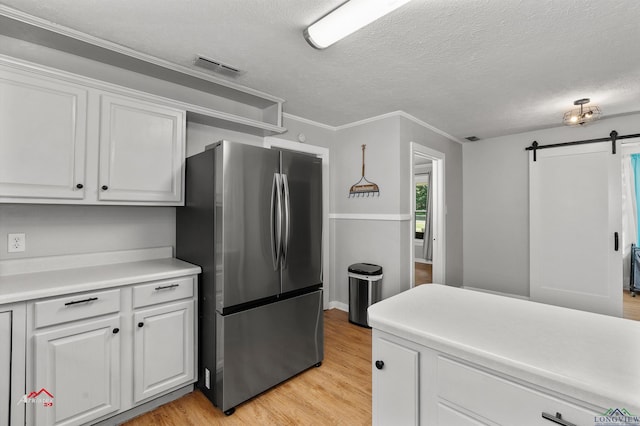 kitchen featuring white cabinetry, a barn door, light hardwood / wood-style flooring, stainless steel fridge, and a textured ceiling