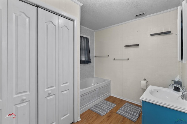 bathroom featuring hardwood / wood-style floors, vanity, crown molding, a tub to relax in, and a textured ceiling