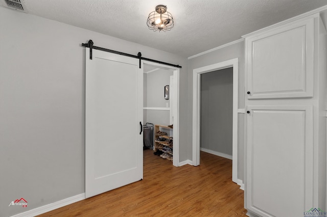 corridor featuring a barn door, a textured ceiling, and light hardwood / wood-style flooring